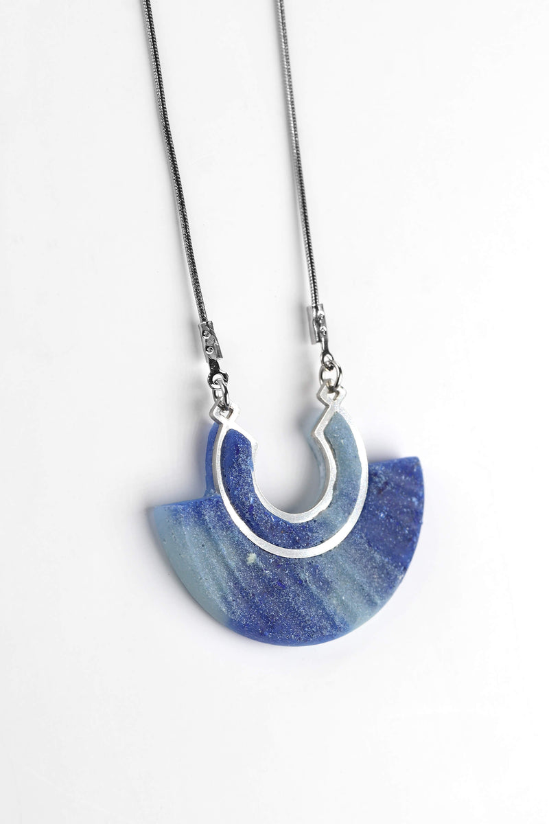 Le collier pendentif Aurore, en résine écologique de couleur bleu indigo et chaîne en acier inoxydable hypoallergénique, fabrication artisanale