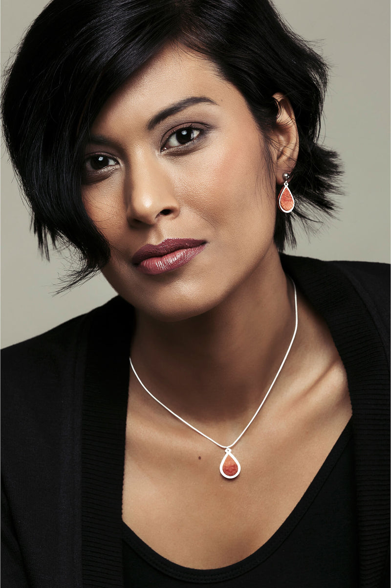 Short dark-haired fashion model woman wearing Candide jewelry set parure with earrings studs and teardrop adjustable length necklace in red coral color resin and hypoallergenic stainless steel