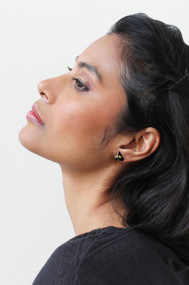 Dark haired fashion model woman wearing Diamant, small triangular earrings in black   eco-friendly resin with 24 carats gold leaf, hypoallergenic stainless steel studs and gold leaf