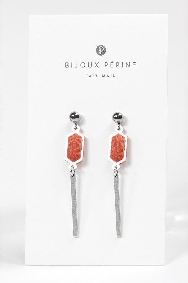 modèle portant les boucles d'oreilles Nova, fabriquées à la main par Bijoux Pépine, en rouge corail, en résine écologique et en acier inoxydable.
