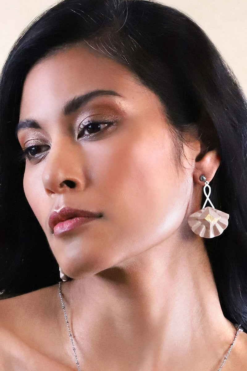 Woman wearing Statement earrings studs in stainless steal and gold leaf 24 carats named Cancan and beige color