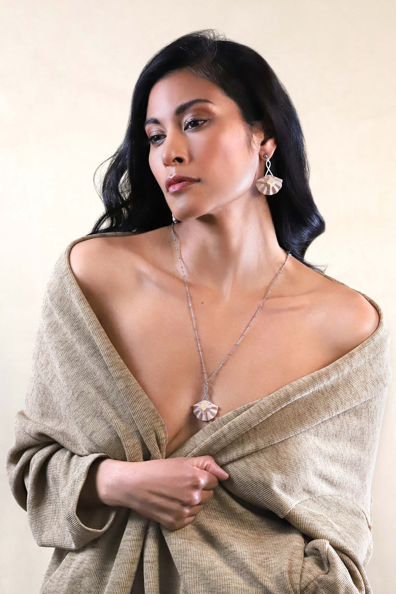 Woman wearing the handmade statement jewelry set with long pendant chain in stainless steal and studs earrings with gold leaf 24 carats named Cancan and beige resin color