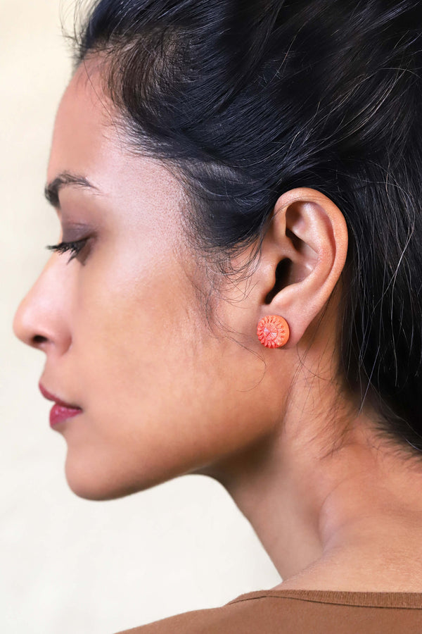 Modèle femme brune portant Altaïr boucles d'oreilles clous d'oreilles forme ronde acier inoxydable hypoallergénique résine couleur rouge corail