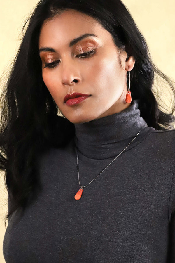Dark haired model fashion woman wearing Rosée jewellery set parure with earrings sand teardrop adjustable length necklace in coral red color resin and hypoallergenic stainless steel
