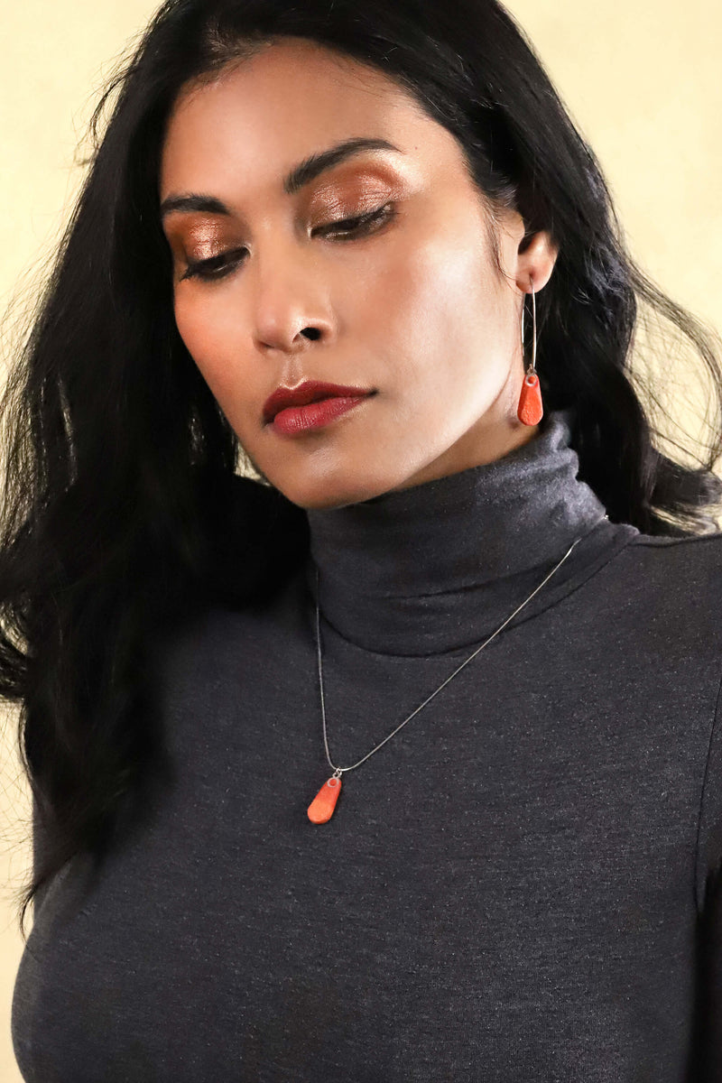 Modèle féminin de mode portant un collier à longueur réglable en résine durable et acier inoxydable hypoallergénique de couleur rouge corail et orange.
